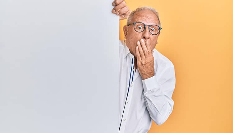 Senior man hiding behind a white board.