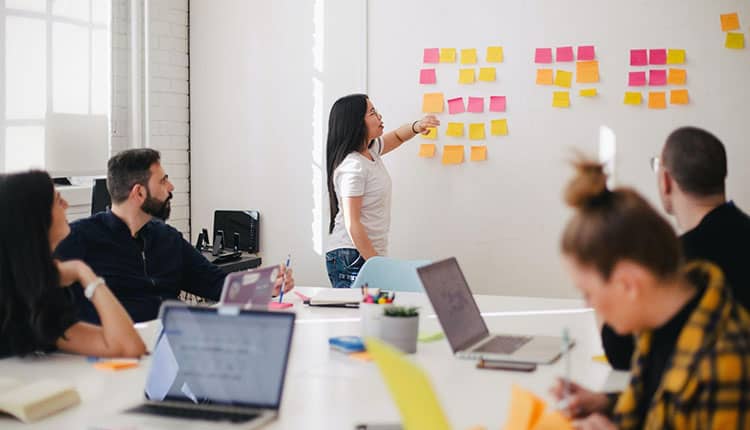 A group of people in a meeting room with sticky notes on the wall.