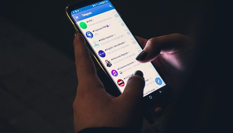 Person using telegram messaging app on smartphone in a dimly lit environment.