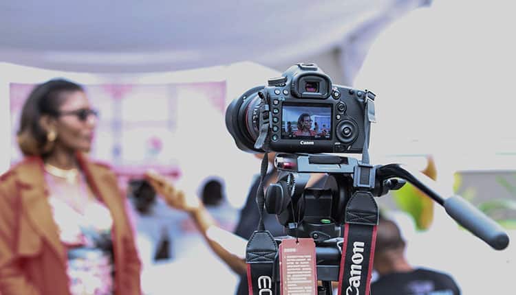 A dslr camera set up on a tripod capturing a woman in focus in the background.