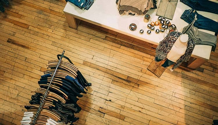 Overhead view of a clothing store with racks of clothes, accessories on a table, and a mannequin wearing a scarf.