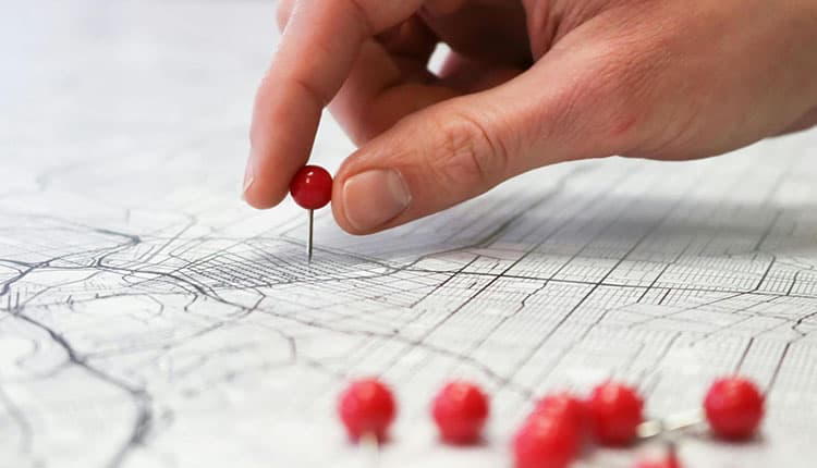 A hand presses a red pin into a map.