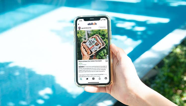 A hand holds a smartphone displaying an Instagram post featuring a pack of Beyond Meat Hot Italian Sausages near a swimming pool.