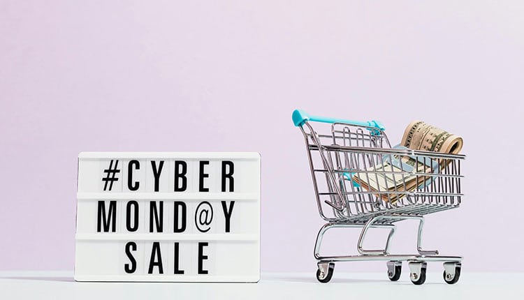 Lightbox sign with the text "#CYBER MONDAY SALE" next to a small shopping cart containing rolls of dollar bills.