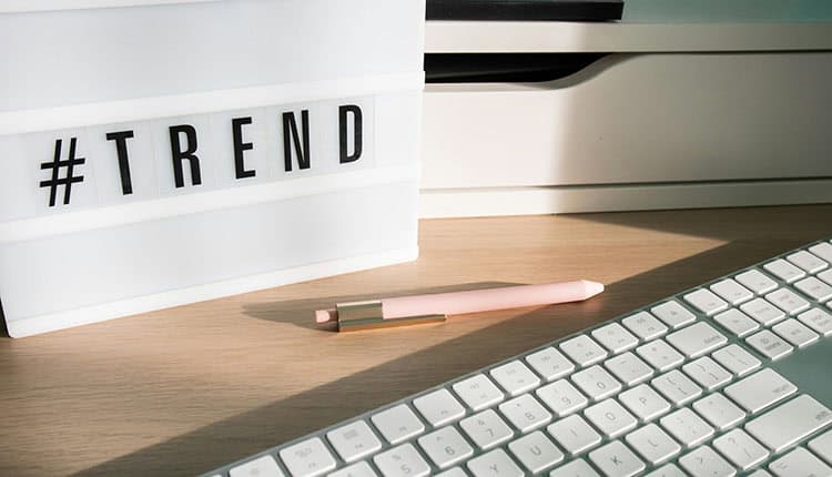 A white lightbox with "#TREND" in black letters is on a wooden desk next to a pink pen and a white keyboard.