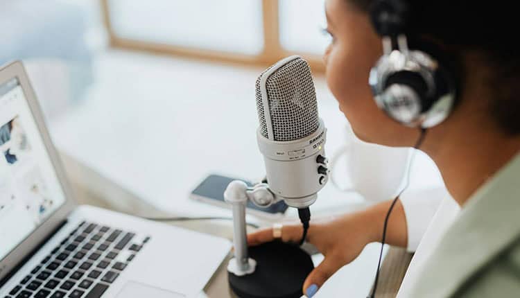 Person wearing headphones speaks into a microphone near a laptop.