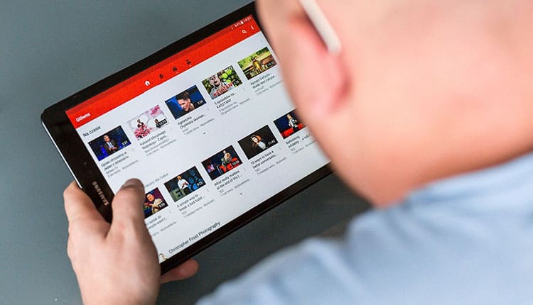 Person browsing a YouTube channel on a tablet with various video thumbnails visible.