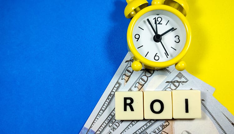 A yellow clock on top of US dollar bills with letter tiles spelling "ROI" on a blue and yellow background.