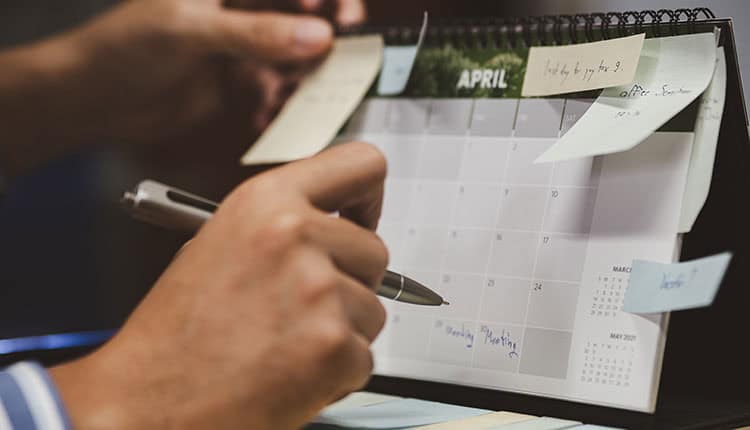 Person writing on a desk calendar for April, surrounded by sticky notes.