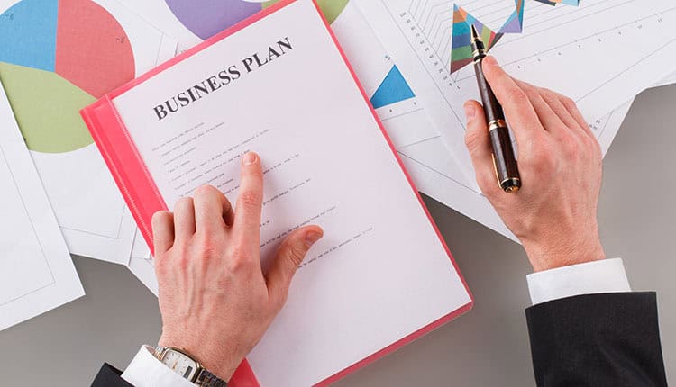 Person reviewing a business plan document with charts and graphs scattered on a table.