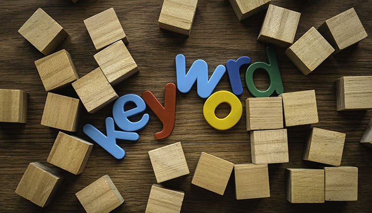 Wooden blocks scattered around colorful letters spelling "keyword" on a wooden surface.