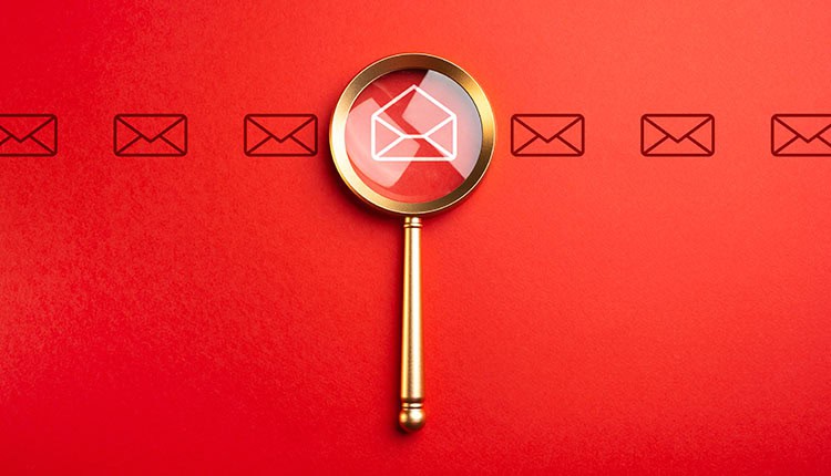 A magnifying glass focuses on a white envelope icon among a row of envelope icons on a red background.