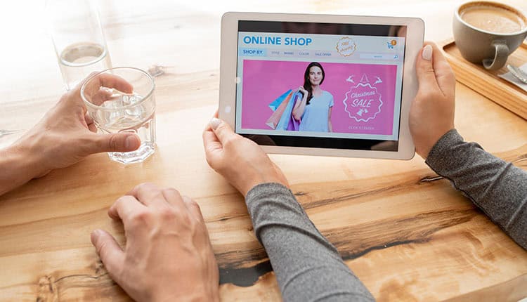 Two people sitting at a wooden table view an online shop on a tablet