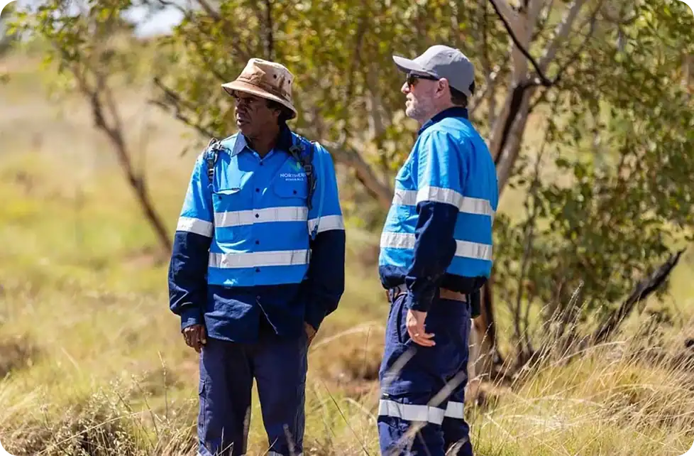 Two people in blue work uniforms and hats standing in a field.
